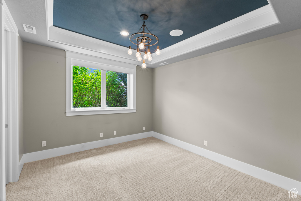 Carpeted empty room featuring a raised ceiling, a chandelier, and baseboards