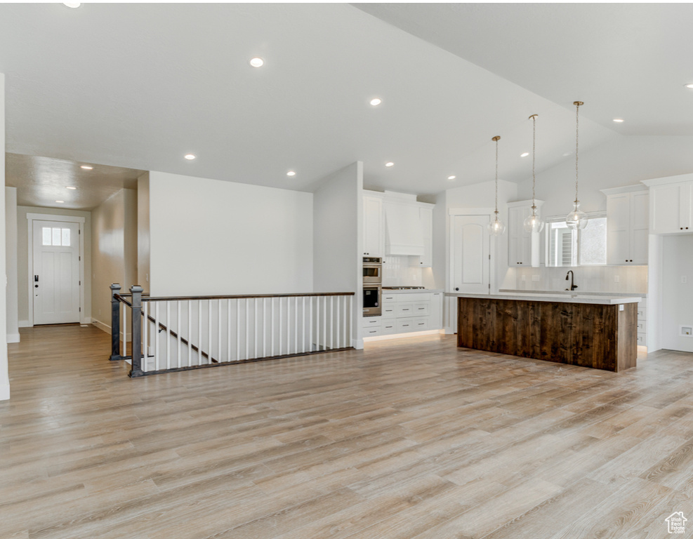 Kitchen with tasteful backsplash, white cabinets, vaulted ceiling, light wood-type flooring, and light countertops