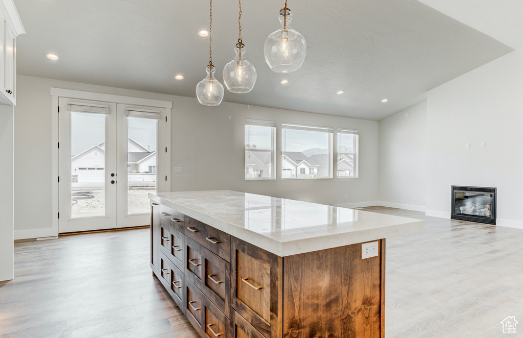 Kitchen with light wood-style floors, a glass covered fireplace, french doors, recessed lighting, and white cabinetry