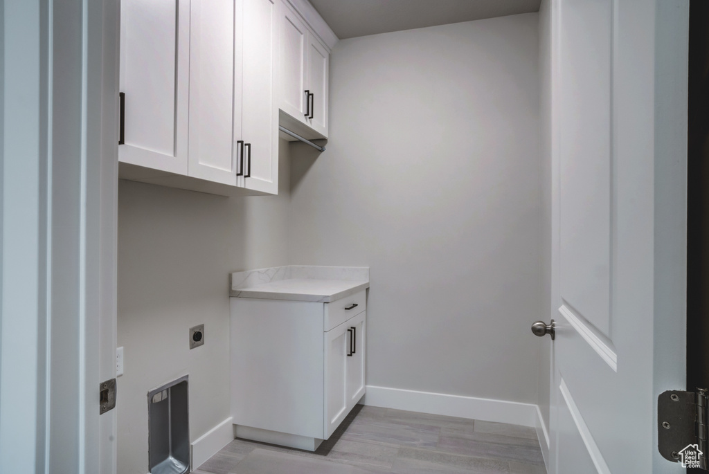 Clothes washing area with hookup for an electric dryer, baseboards, light wood-type flooring, and cabinet space