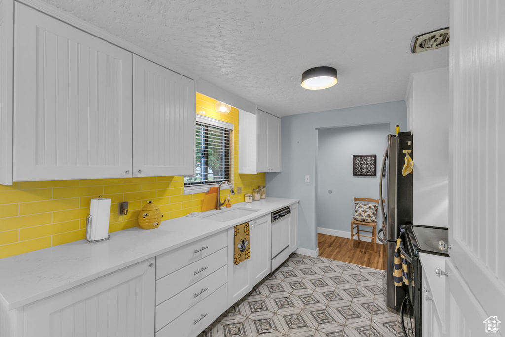 Kitchen with a sink, black range with electric cooktop, dishwasher, baseboards, and white cabinetry