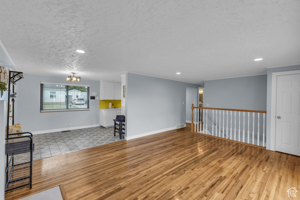 Unfurnished living room with a textured ceiling, wood finished floors, a chandelier, baseboards, and recessed lighting