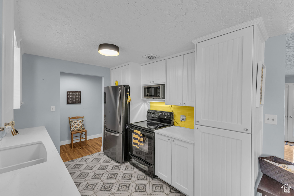 Kitchen featuring appliances with stainless steel finishes, light countertops, white cabinets, a sink, and a textured ceiling