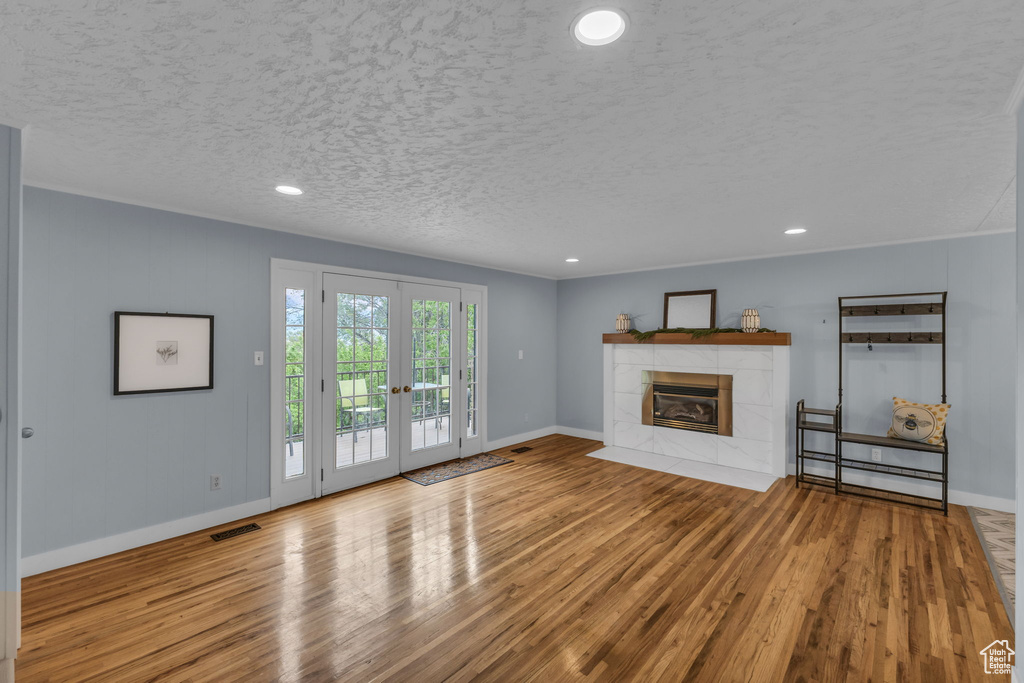 Unfurnished living room with baseboards, wood finished floors, french doors, a tiled fireplace, and recessed lighting