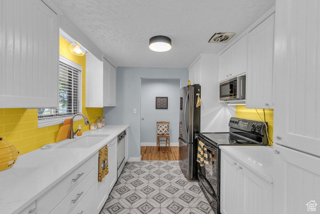 Kitchen featuring appliances with stainless steel finishes, a sink, white cabinetry, baseboards, and a textured ceiling