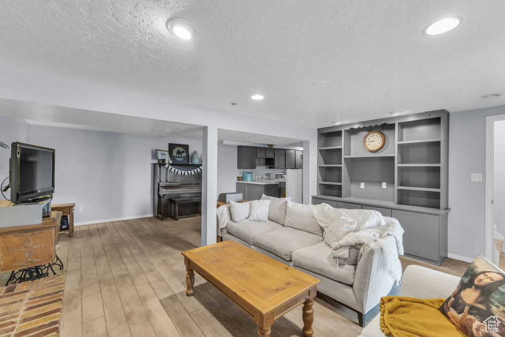 Living room featuring a textured ceiling, baseboards, recessed lighting, and light wood-style flooring