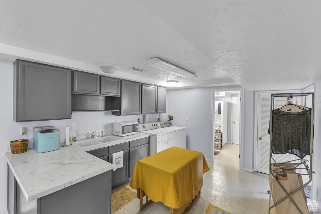 Kitchen featuring white microwave, a sink, washing machine and dryer, gray cabinetry, and a textured ceiling