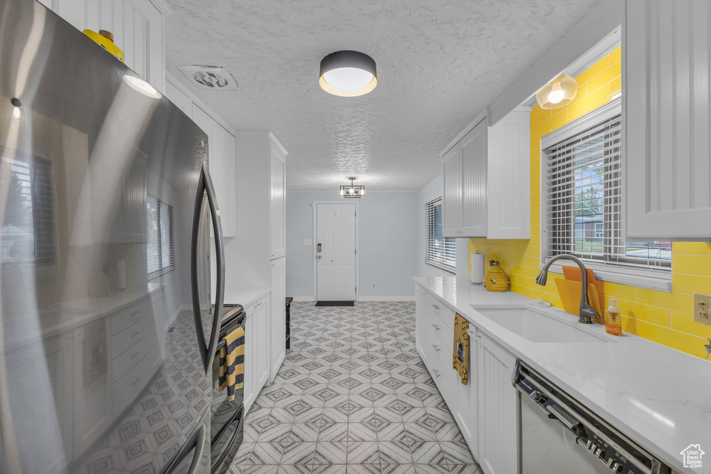 Kitchen featuring freestanding refrigerator, dishwashing machine, a sink, white cabinetry, and light floors