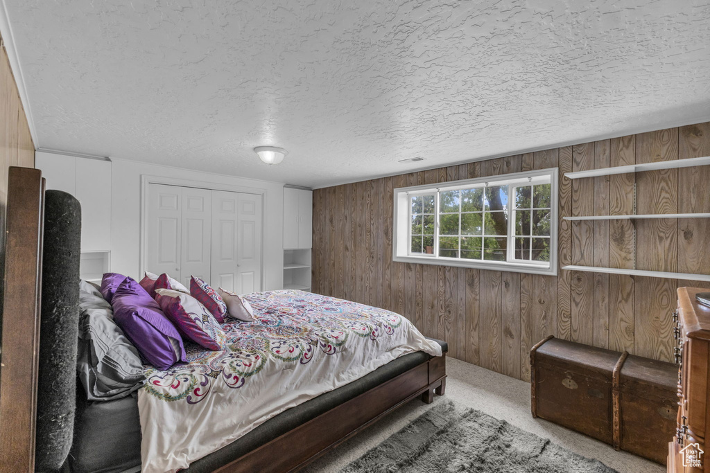 Carpeted bedroom featuring wood walls, a textured ceiling, and a closet