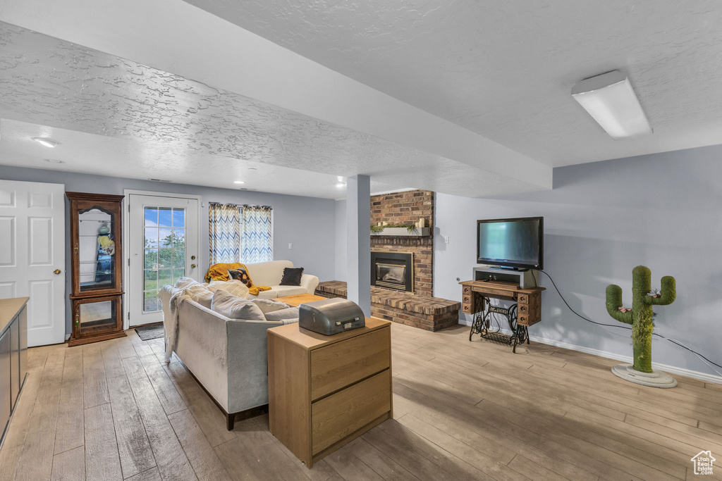 Living area featuring a textured ceiling, light wood finished floors, a brick fireplace, and baseboards