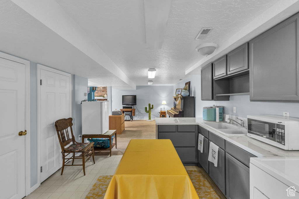 Kitchen featuring white microwave, gray cabinets, a sink, light countertops, and a textured ceiling