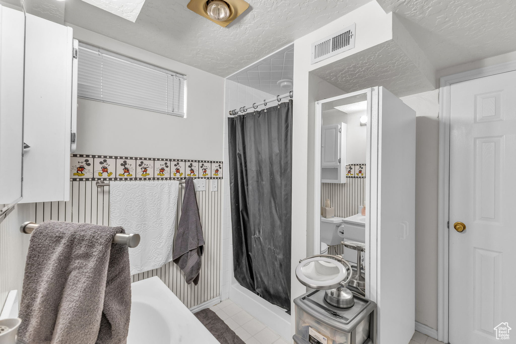 Full bathroom featuring curtained shower, a textured ceiling, tile patterned floors, and baseboards