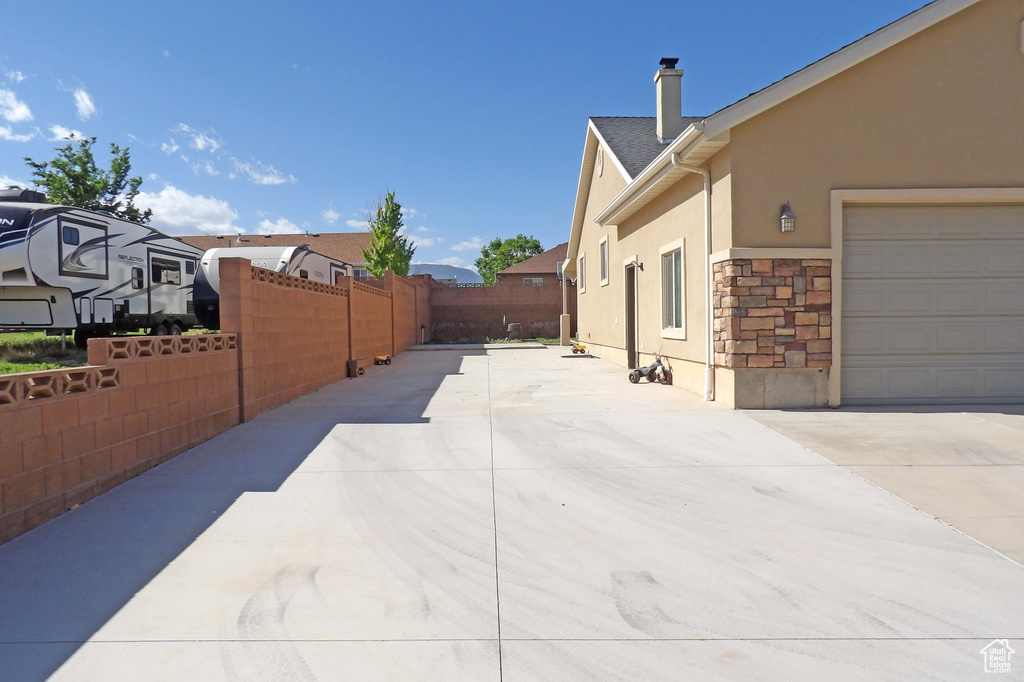 View of side of home featuring stucco siding, fence, stone siding, and driveway