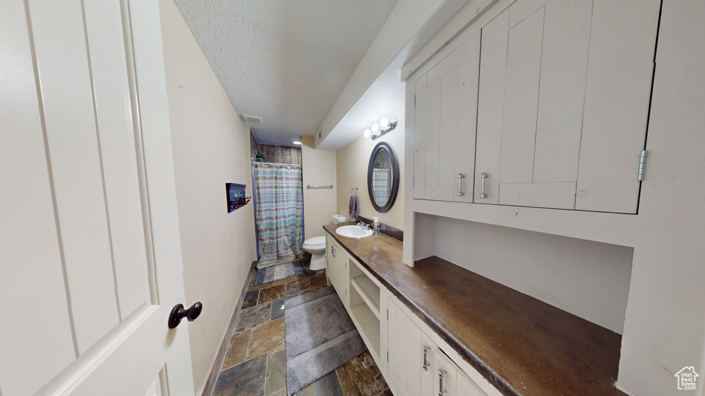 Bathroom featuring stone tile floors, toilet, vanity, curtained shower, and a textured ceiling