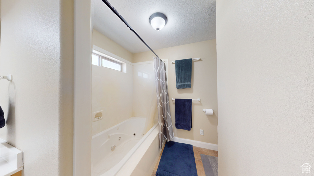 Bathroom featuring baseboards, a combined bath / shower with jetted tub, and a textured ceiling