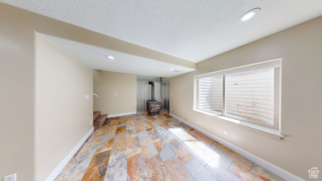 Unfurnished living room with a wood stove, baseboards, light stone finish flooring, a textured ceiling, and recessed lighting