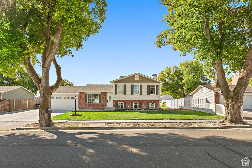 Split level home with brick siding, an attached garage, concrete driveway, and a chimney