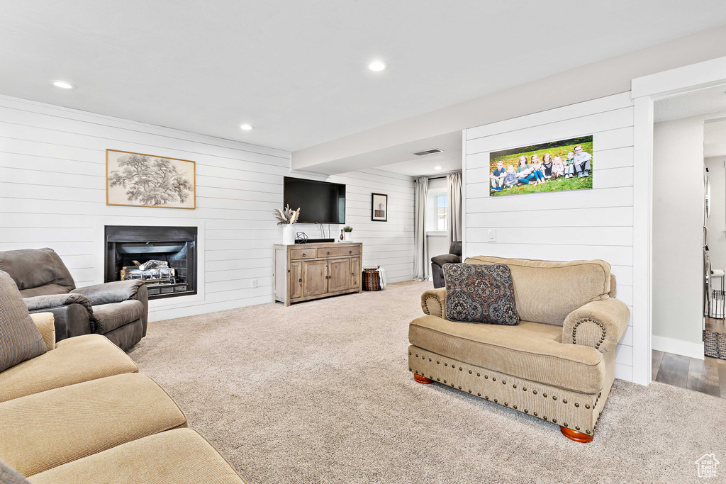 Carpeted living area with wood walls, recessed lighting, and a glass covered fireplace