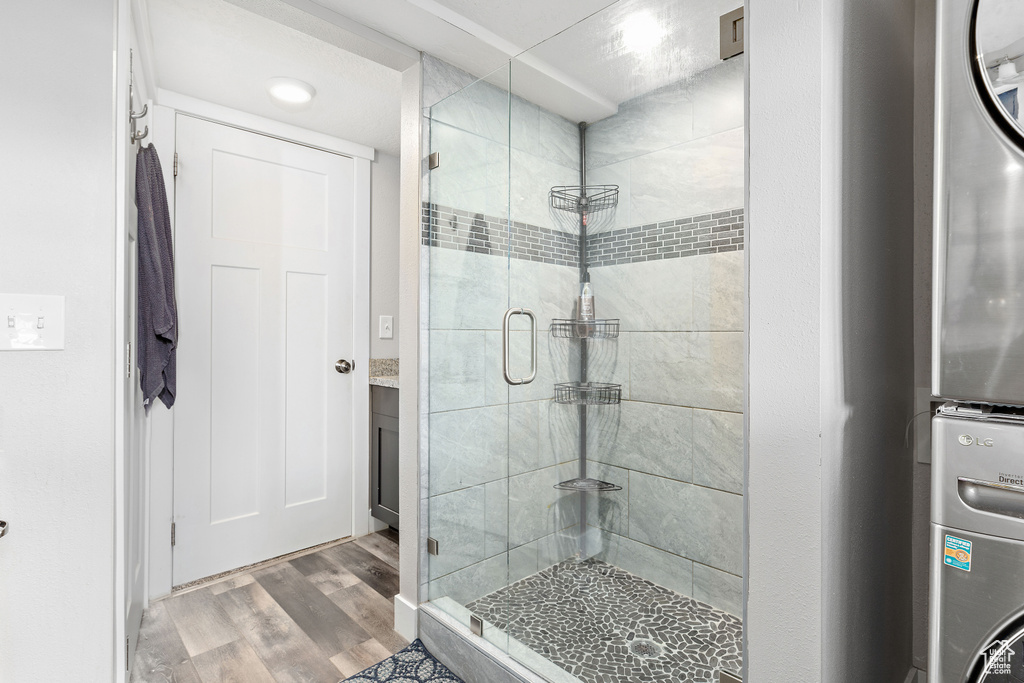 Full bath with a shower stall, stacked washer / dryer, and wood finished floors