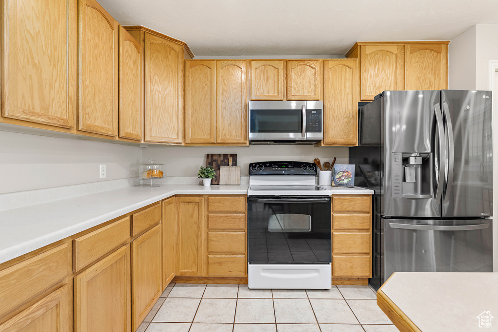 Kitchen with stainless steel appliances, light tile patterned flooring, light countertops, and light brown cabinetry