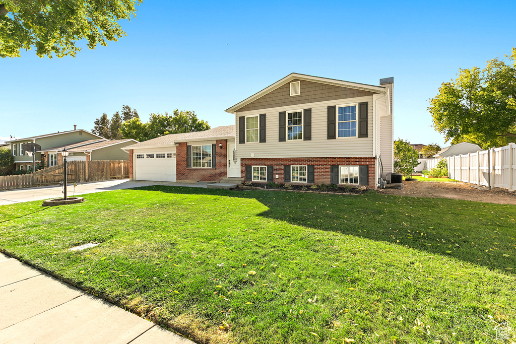Tri-level home with an attached garage, brick siding, concrete driveway, and central air condition unit
