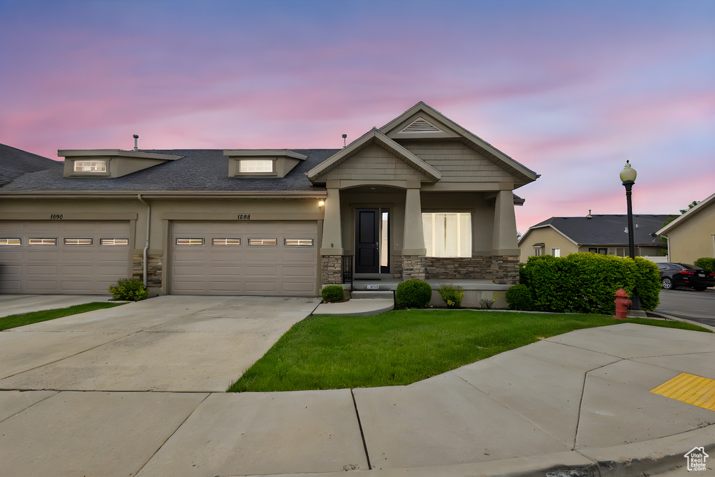 View of front facade featuring stone siding, driveway, a lawn, stucco siding, and an attached garage