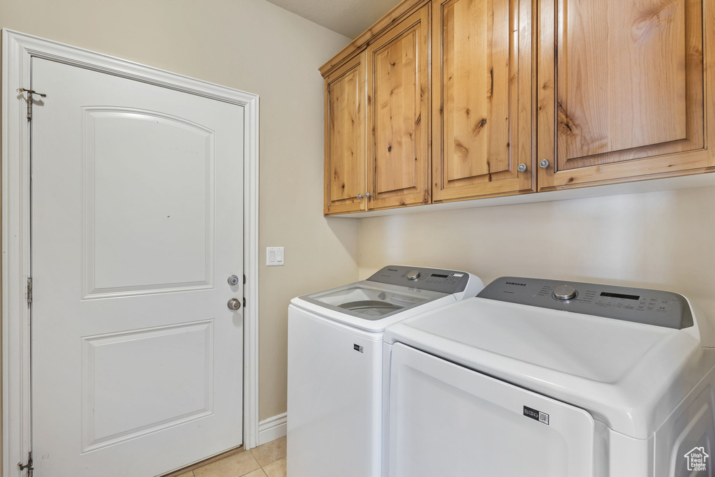 Washroom featuring independent washer and dryer, cabinet space, light tile patterned flooring, and baseboards