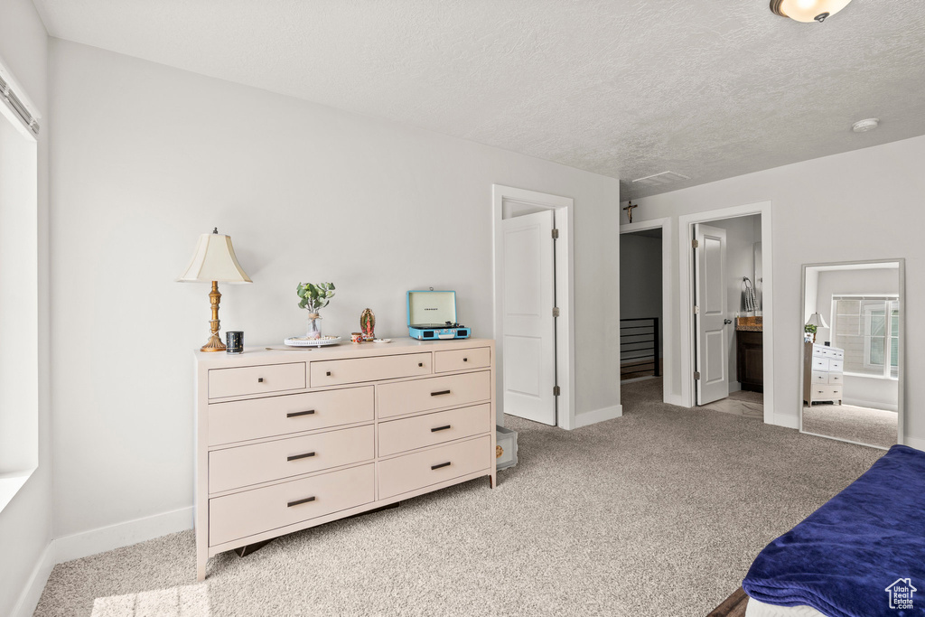 Bedroom with light carpet, baseboards, a textured ceiling, and ensuite bath
