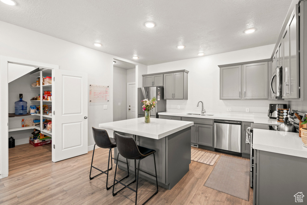 Kitchen featuring stainless steel appliances, gray cabinetry, a breakfast bar area, light wood finished floors, and a sink