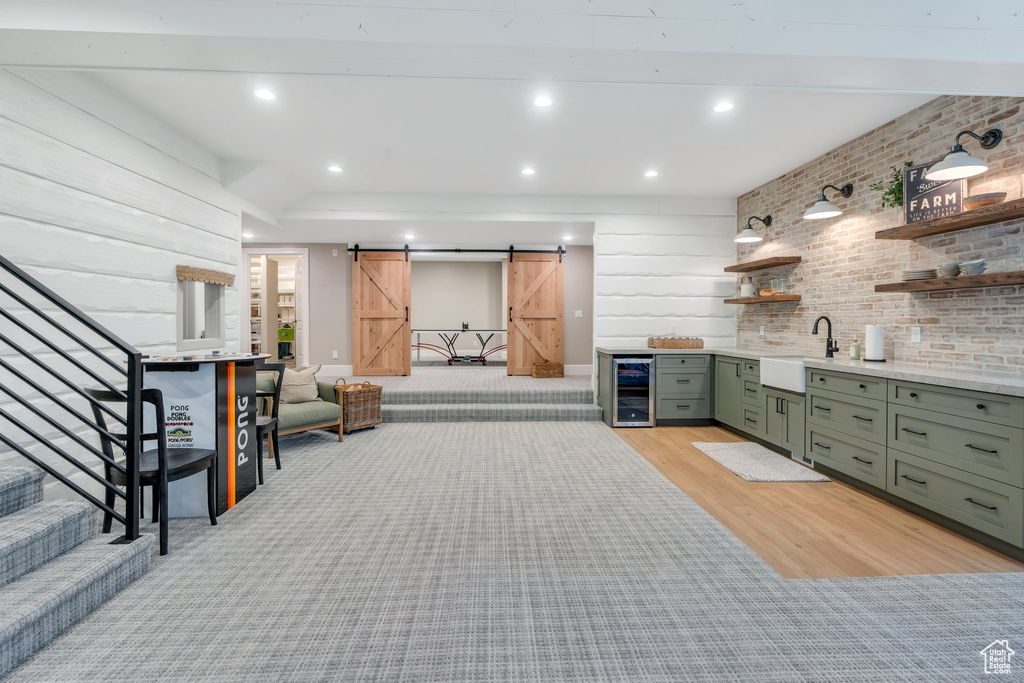 Bar area with wine cooler, a barn door, a sink, stairs, and light wood-type flooring