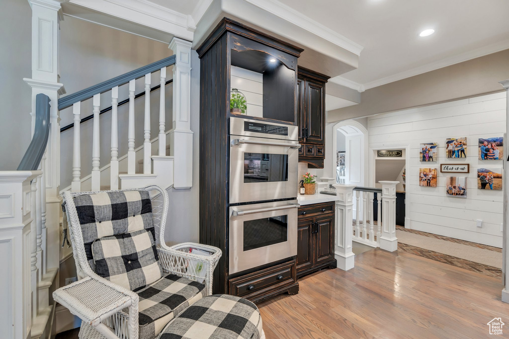 Kitchen with stainless steel double oven, light wood finished floors, dark brown cabinets, crown molding, and recessed lighting