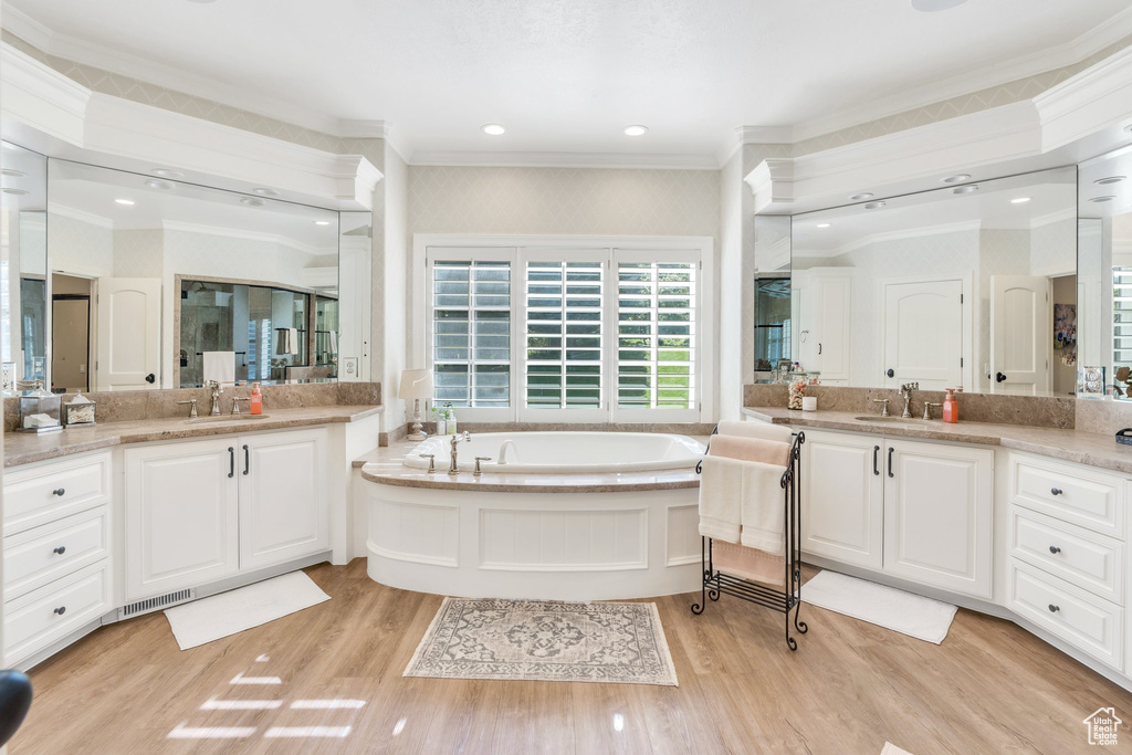 Bathroom with ornamental molding, wood finished floors, a bath, and two vanities