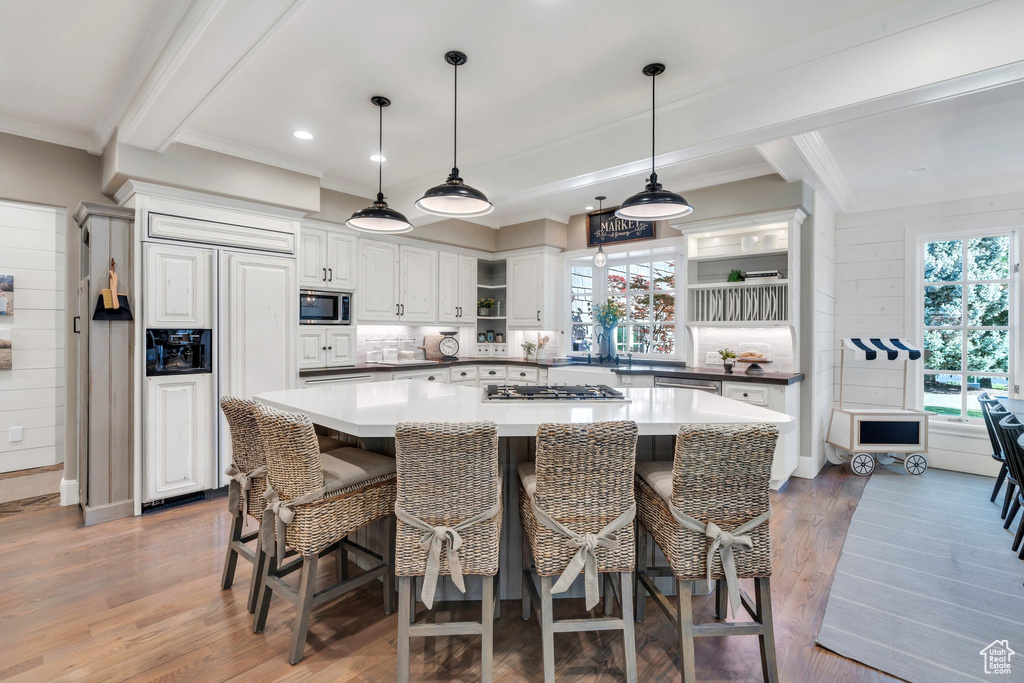 Kitchen featuring built in appliances, ornamental molding, open shelves, wood finished floors, and white cabinetry