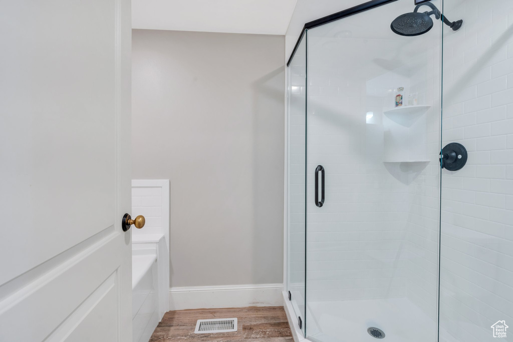 Bathroom with a stall shower, wood finished floors, a garden tub, and baseboards