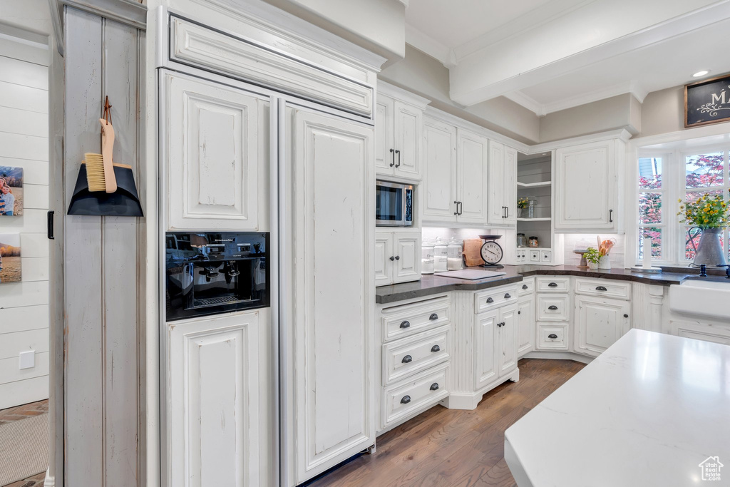 Kitchen with stainless steel microwave, paneled fridge, open shelves, white cabinetry, and crown molding