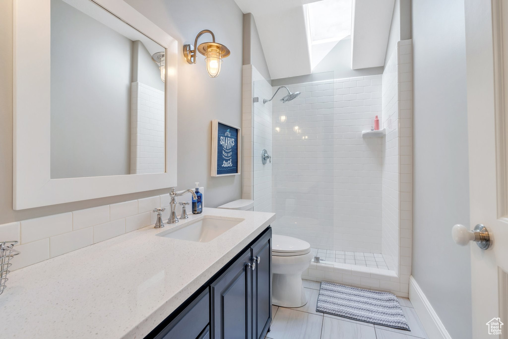 Full bath featuring toilet, tiled shower, vanity, and a skylight