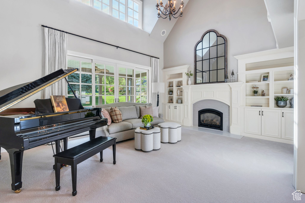 Living room featuring a towering ceiling, carpet, a chandelier, healthy amount of natural light, and a fireplace with raised hearth