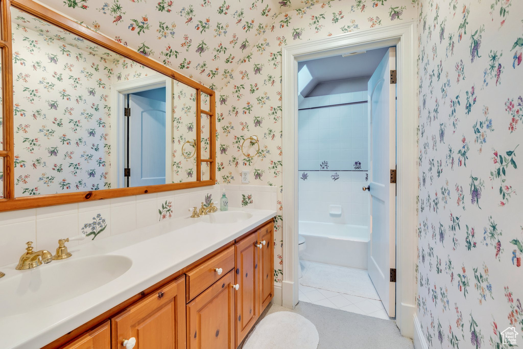 Bathroom with wallpapered walls, tile patterned floors, double vanity, and toilet