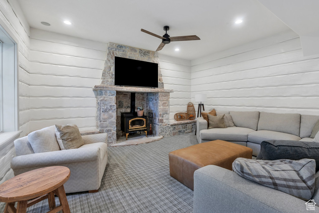 Carpeted living room with a wood stove, a ceiling fan, wooden walls, and recessed lighting