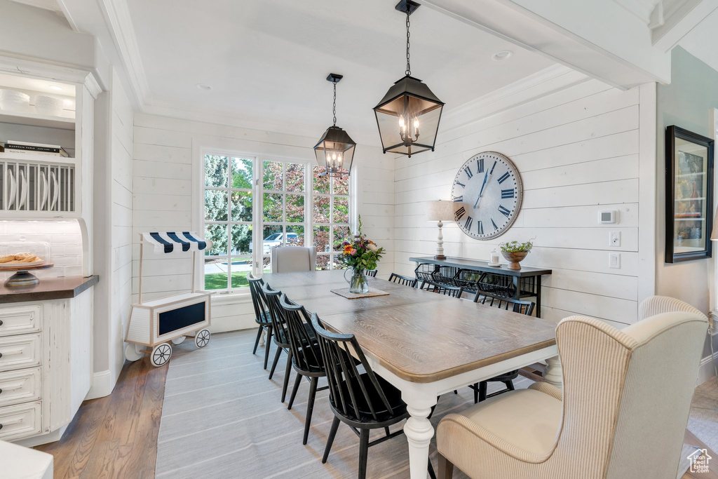 Dining space with a chandelier, wood finished floors, wooden walls, and ornamental molding