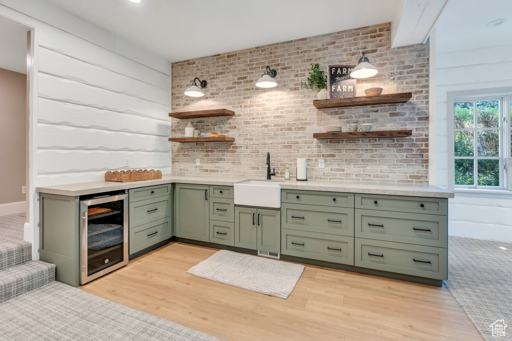Bar featuring beverage cooler, a sink, and light wood finished floors