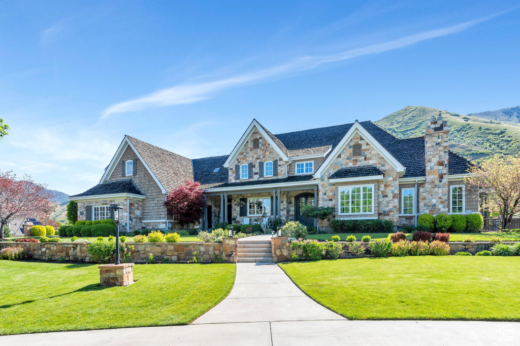 View of front of house featuring stone siding, covered porch, a front yard, and a mountain view