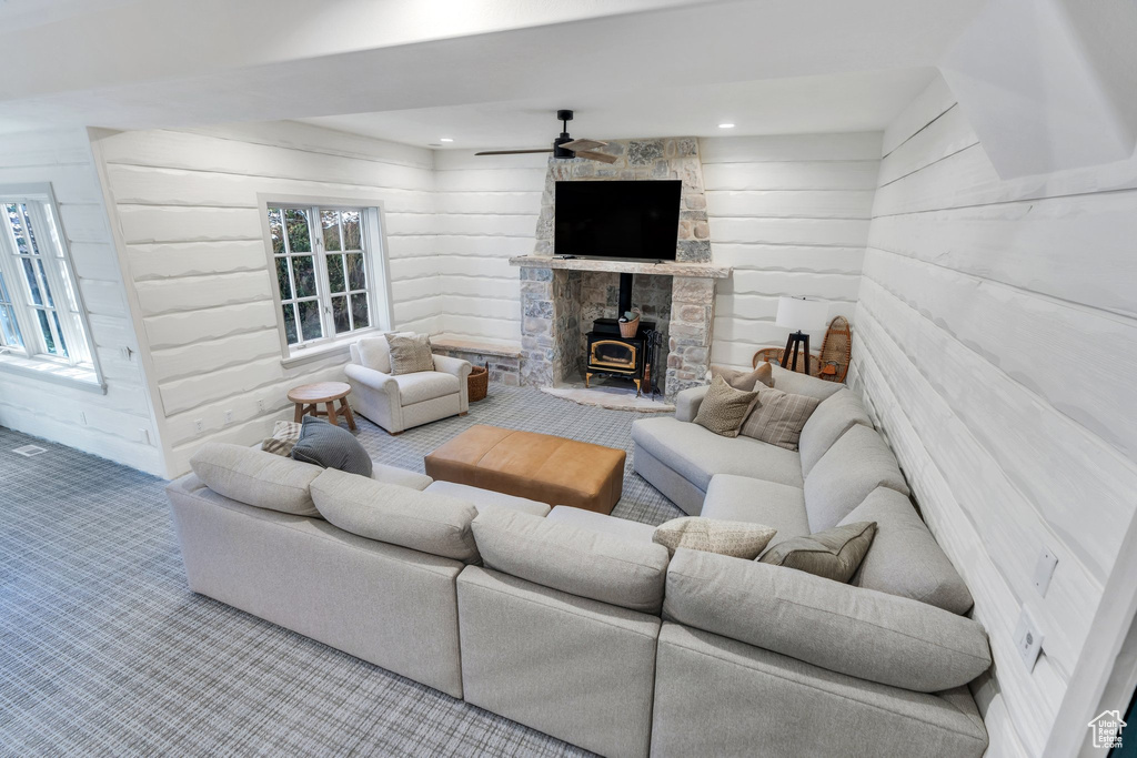 Living area with carpet floors, a wood stove, wood walls, and ceiling fan