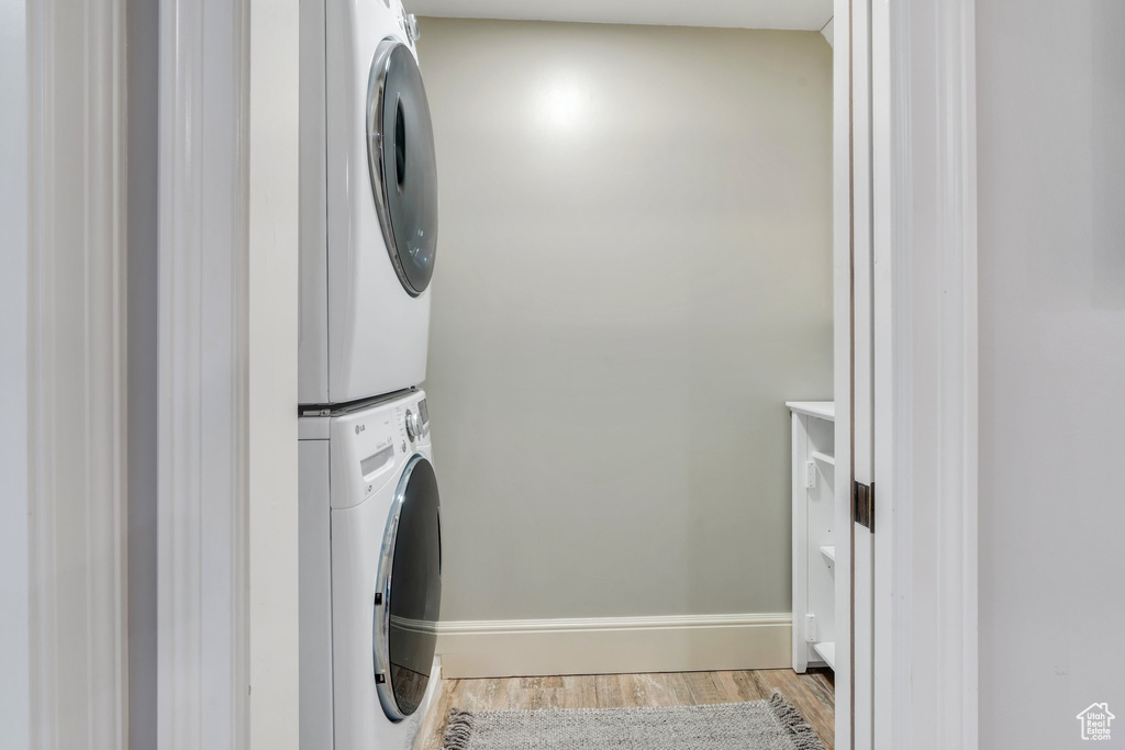 Laundry area featuring stacked washing machine and dryer, light wood finished floors, and baseboards