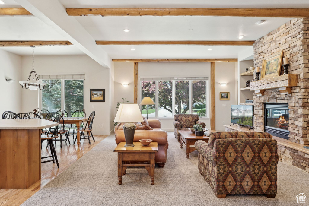 Living area with beam ceiling, a stone fireplace, recessed lighting, a chandelier, and light wood-style flooring