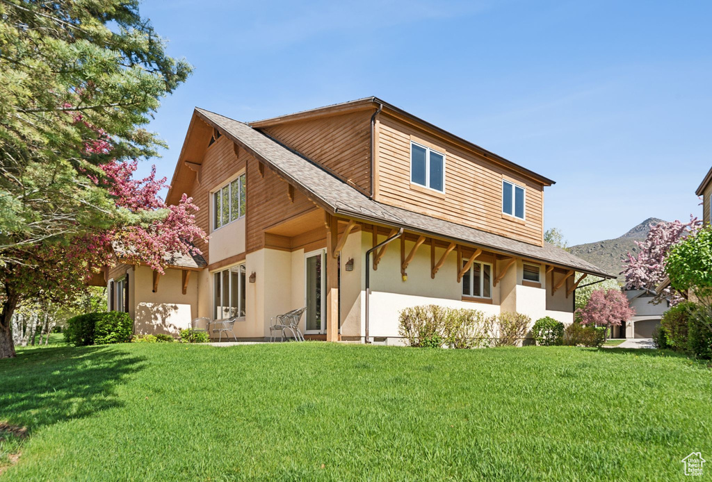 Rear view of property with stucco siding, a yard, and a shingled roof
