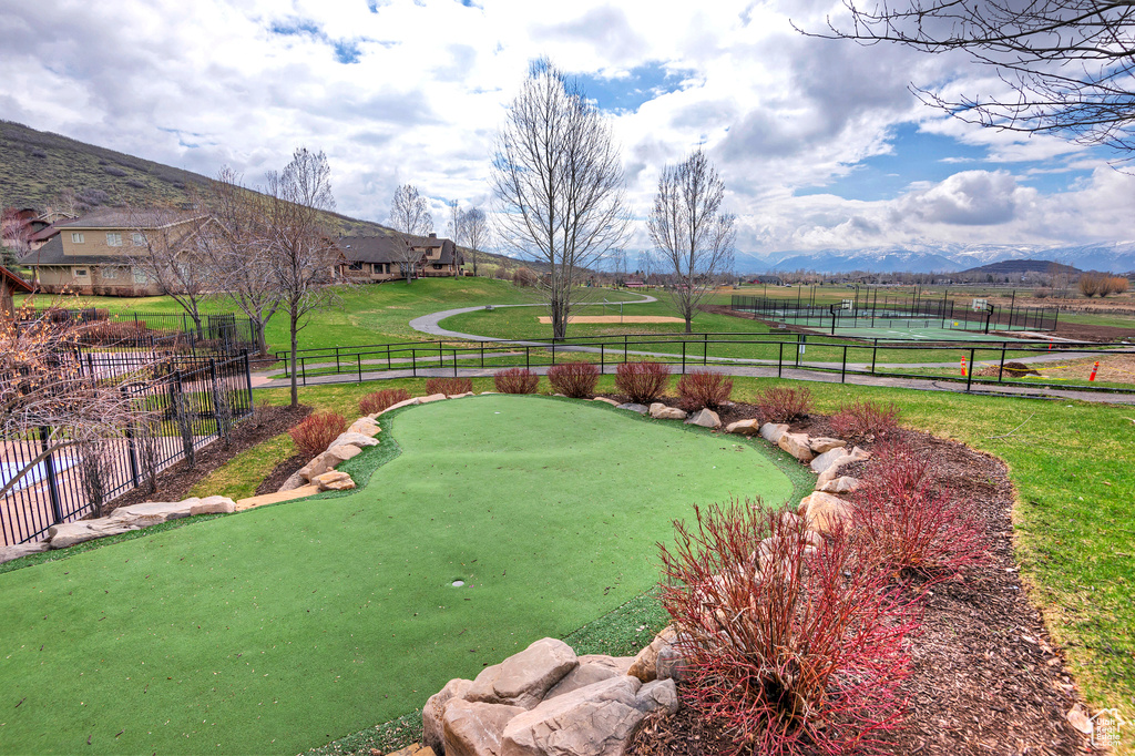 View of yard featuring a putting area, fence, a mountain view, and a tennis court
