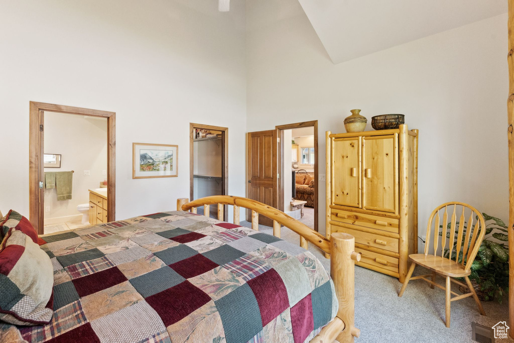 Bedroom with light colored carpet, high vaulted ceiling, and connected bathroom