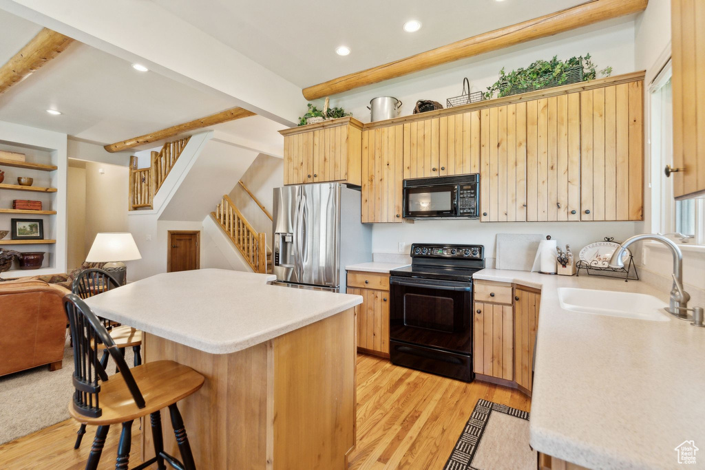 Kitchen featuring black appliances, a sink, a kitchen bar, light wood-style floors, and light brown cabinetry