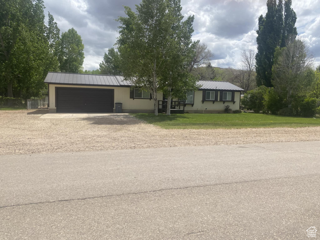 Ranch-style house featuring an attached garage, dirt driveway, metal roof, and a standing seam roof